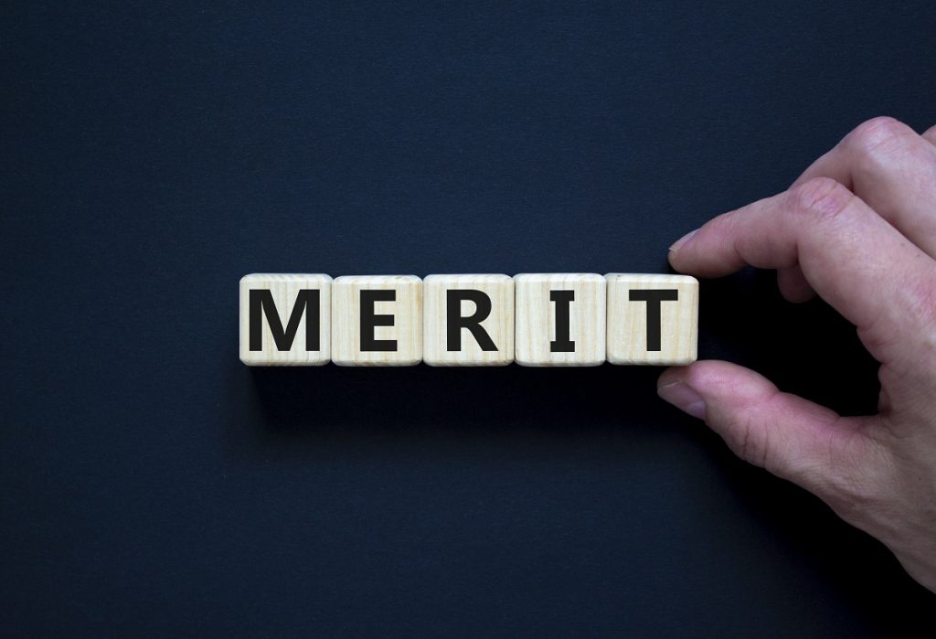 Merit symbol. Wooden cubes with the word 'merit'. Businessman hand. Beautiful black background, copy space. Business and merit concept.
